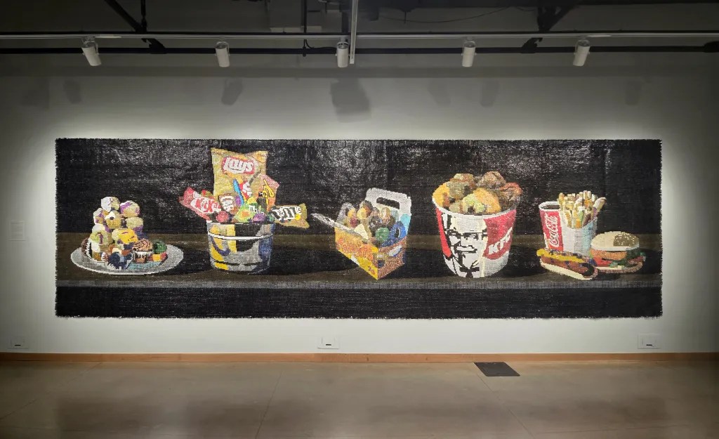 A large mural depicting various fast food items and snacks, including cupcakes on a plate, chips in a bucket, a KFC bucket, fries, and a hamburger.